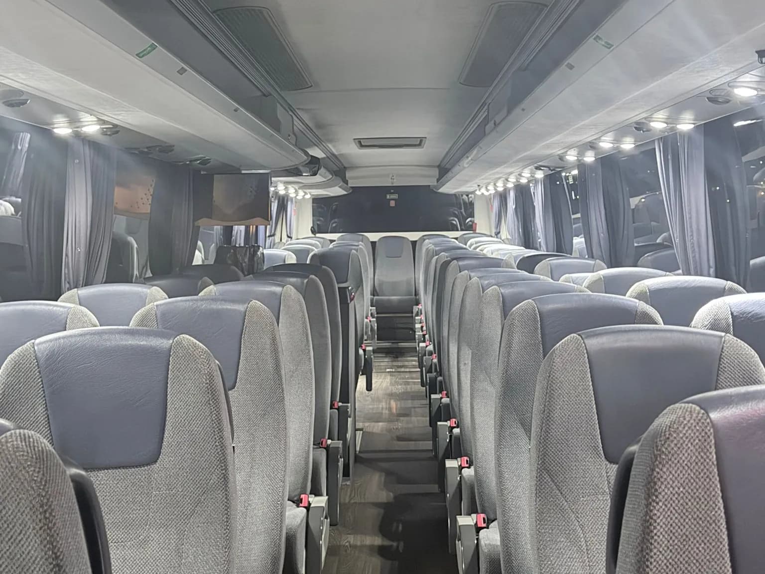 Pasillo central del autocar VDL de 55 plazas de Winking Bus, con butacas reclinables grises de cabecero azul, cortinas y luces de lectura encendidas