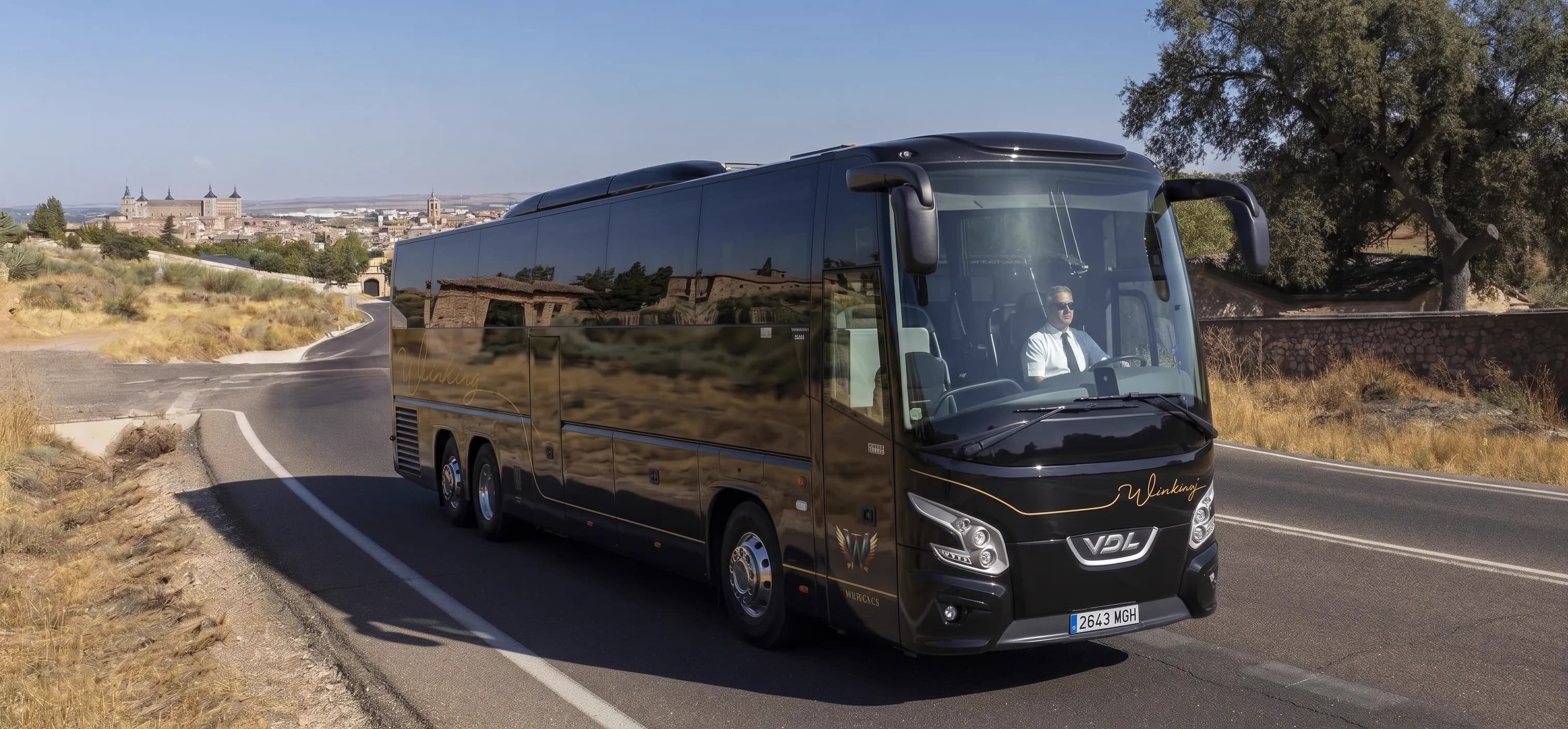 Autocar VDL negro de 70 plazas de Winking Bus, con el conductor al volante, en una carretera con una ciudad al fondo